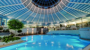 An indoor swimming pool with a modern design, including a glass ceiling and seating areas.
