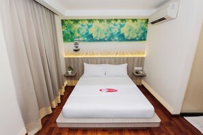 A hotel room with a bed, a painting of a natural scene, a small table with a plant, and an air conditioning unit. - My Hotel @ Kl Sentral (Kuala Lumpur)