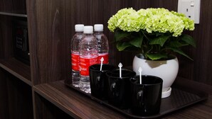 Un mini-bar d’hôtel contenant des bouteilles d’eau, des tasses noires et un hortensia en pot.