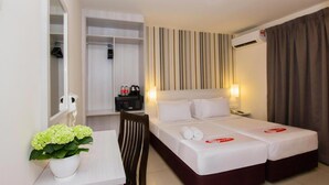Une chambre d’hôtel avec un lit, une table de chevet et un miroir. On aperçoit une plante sur la table et une armoire au fond de la pièce.