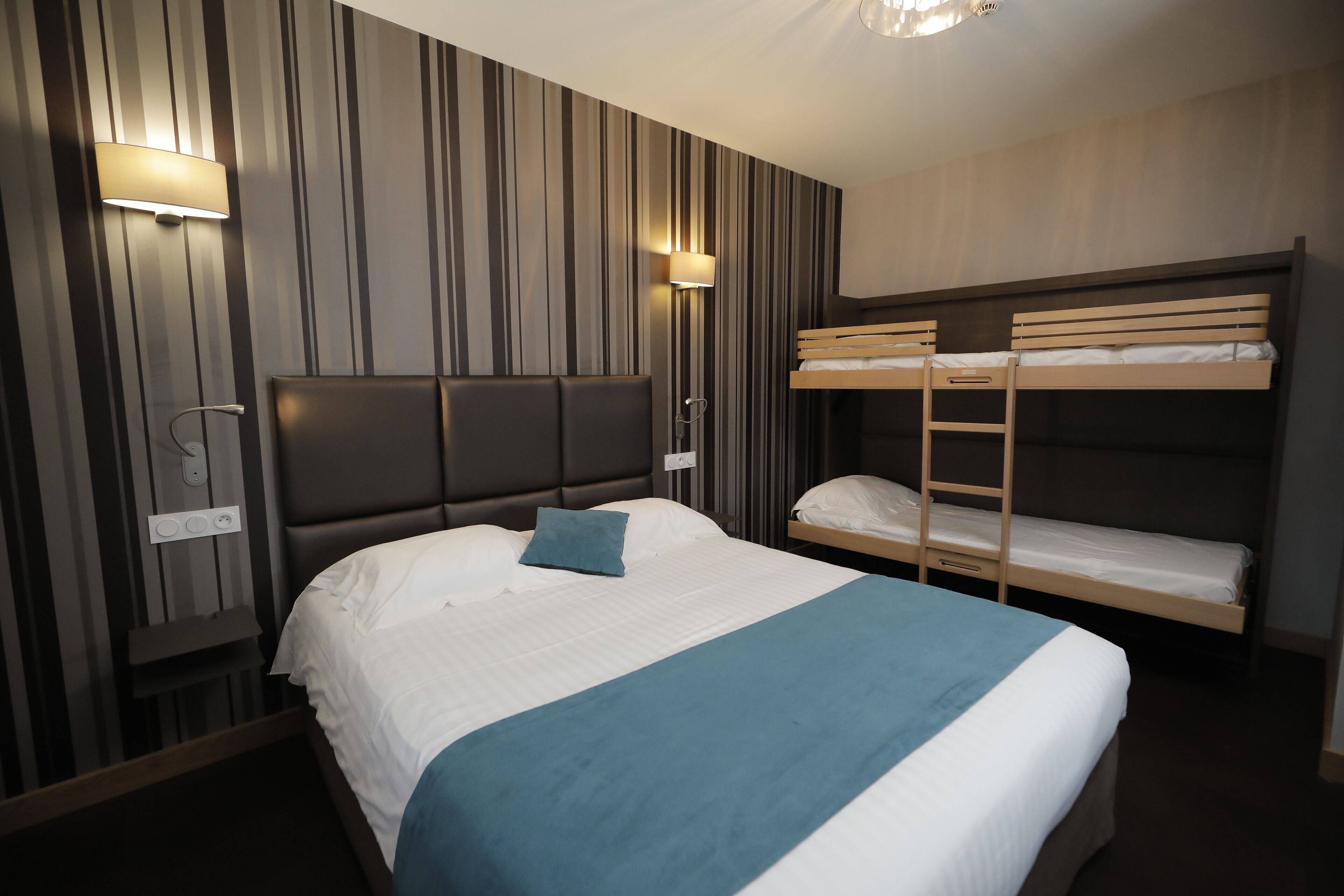 Une chambre d’hôtel avec un grand lit, un lit superposé et une lampe fixée au mur.