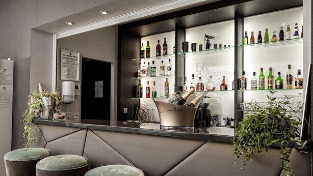 A bar area with a minibar, a variety of liquor bottles, and cushioned bar stools. - Hôtel d'Orléans (Orléans)