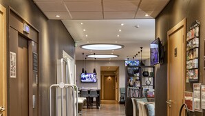 A hotel hallway with a wooden floor, a reception desk, a television, a fire extinguisher, and a vending machine. - Hôtel d'Orléans (Orléans)