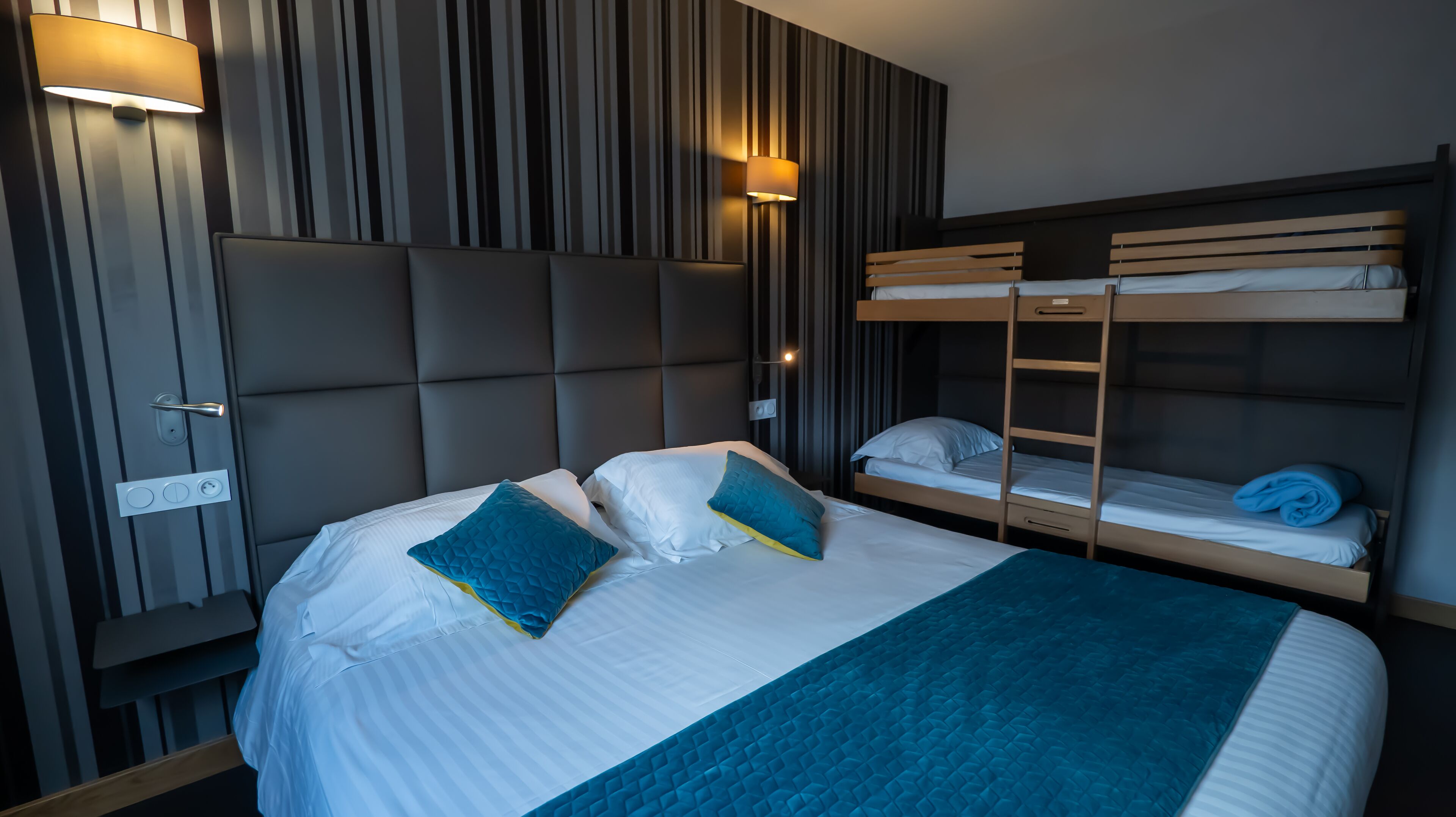 Ein Hotelzimmer mit einem großen Bett, zwei Nachttischen, einem Stockbett und einer Wandleuchte.