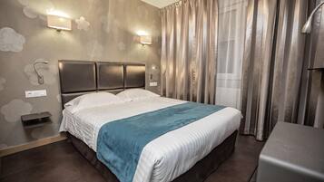 A hotel room with a large bed, a bedside table, a wall-mounted light, and a window with curtains.