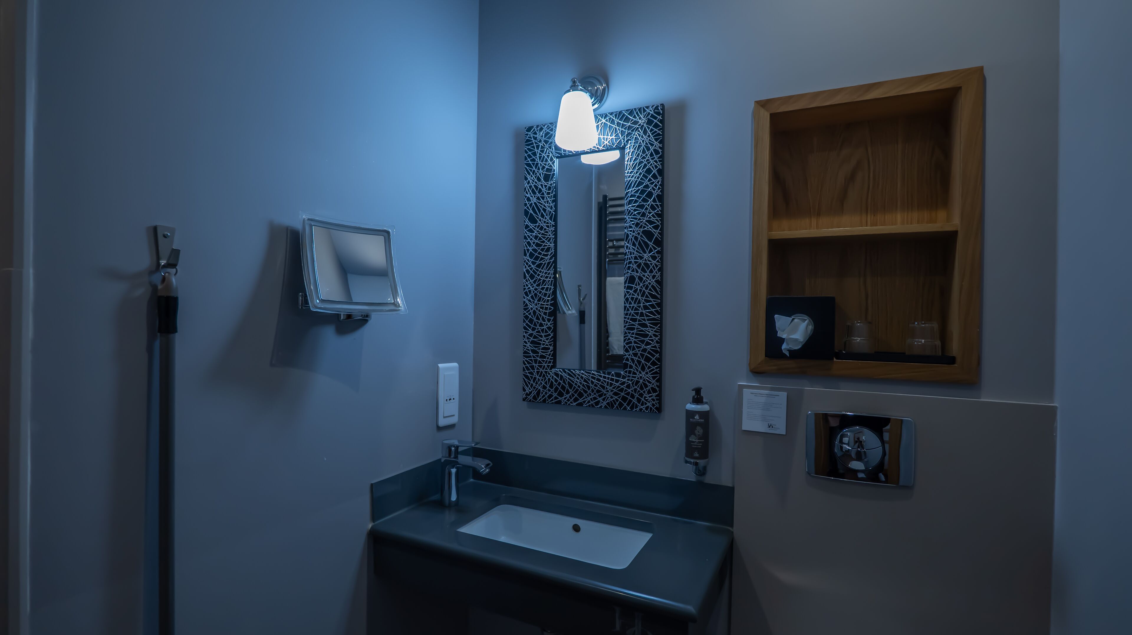 A bathroom with a sink, mirror, and wooden shelf.
