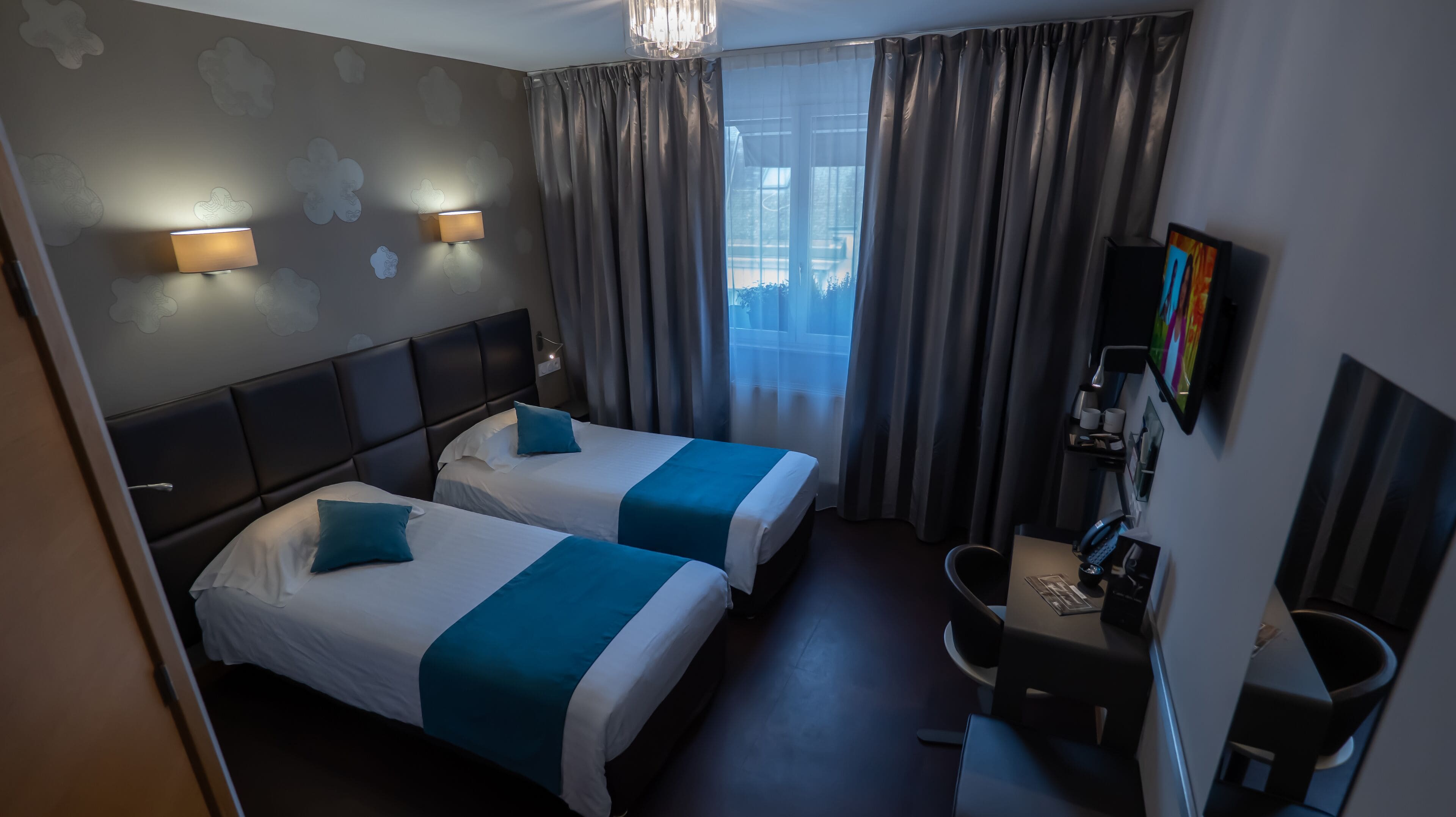 Una habitación de hotel con dos camas, un escritorio, una silla, un televisor y una ventana con cortinas.