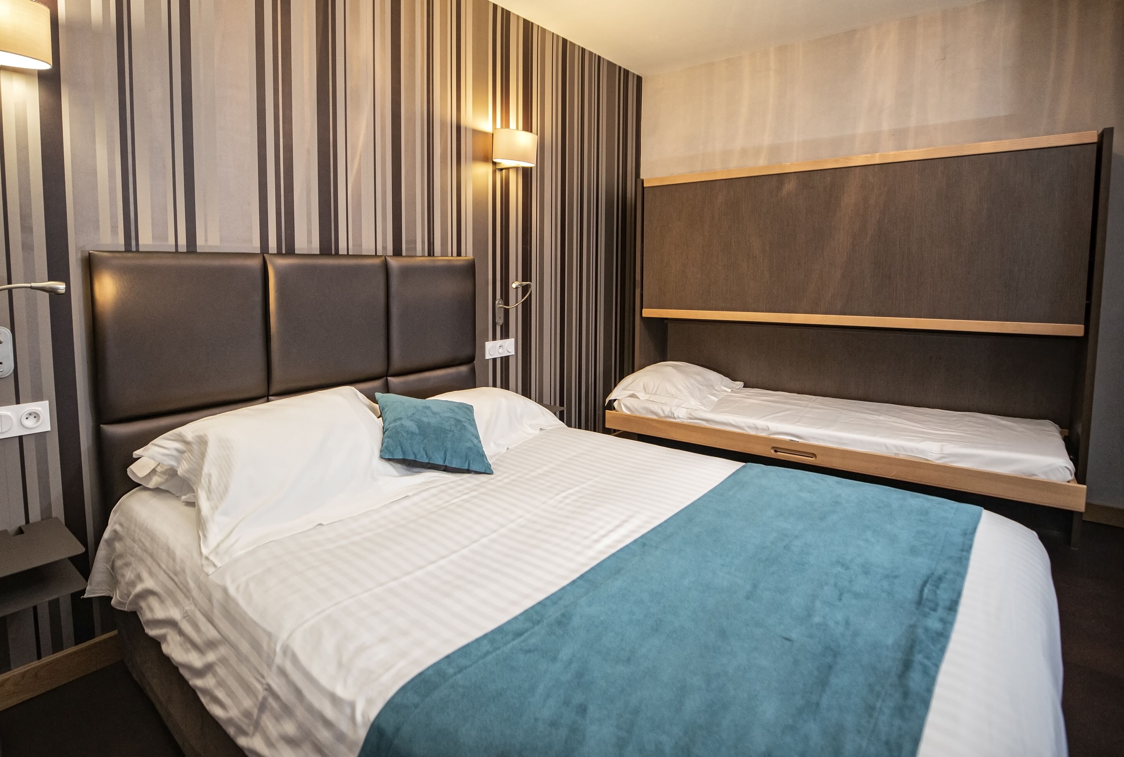 Ein Hotelzimmer mit einem großen Bett, einem kleineren Bett und einer integrierten Sitzbank.