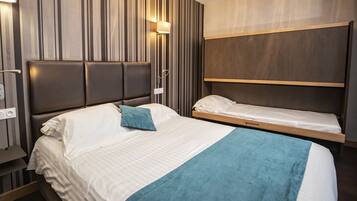 Ein Hotelzimmer mit einem großen Bett, einem kleineren Bett und einer integrierten Sitzbank.