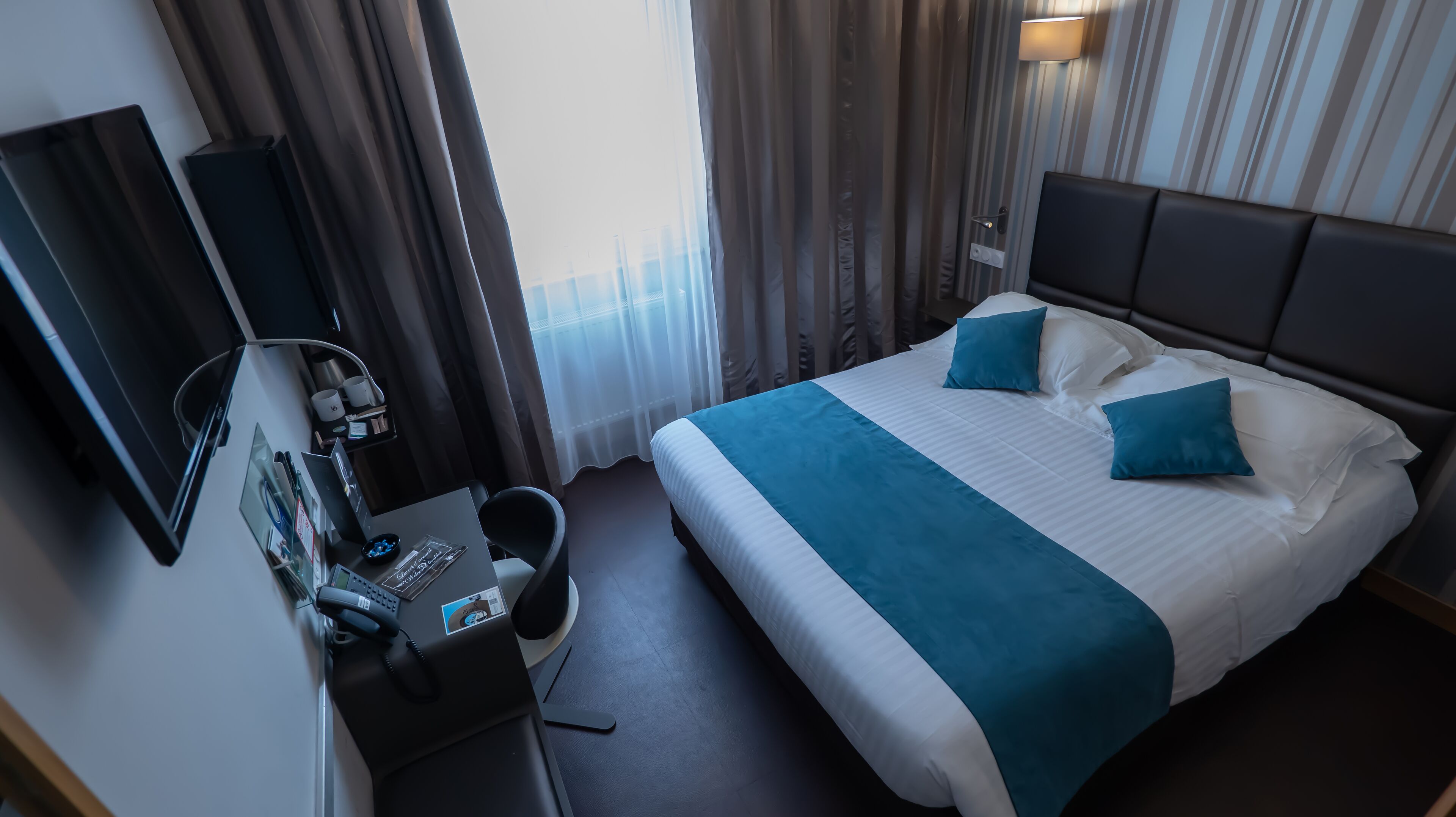 Een hotelkamer met een bed, een bureau met telefoon, een stoel en een televisie.