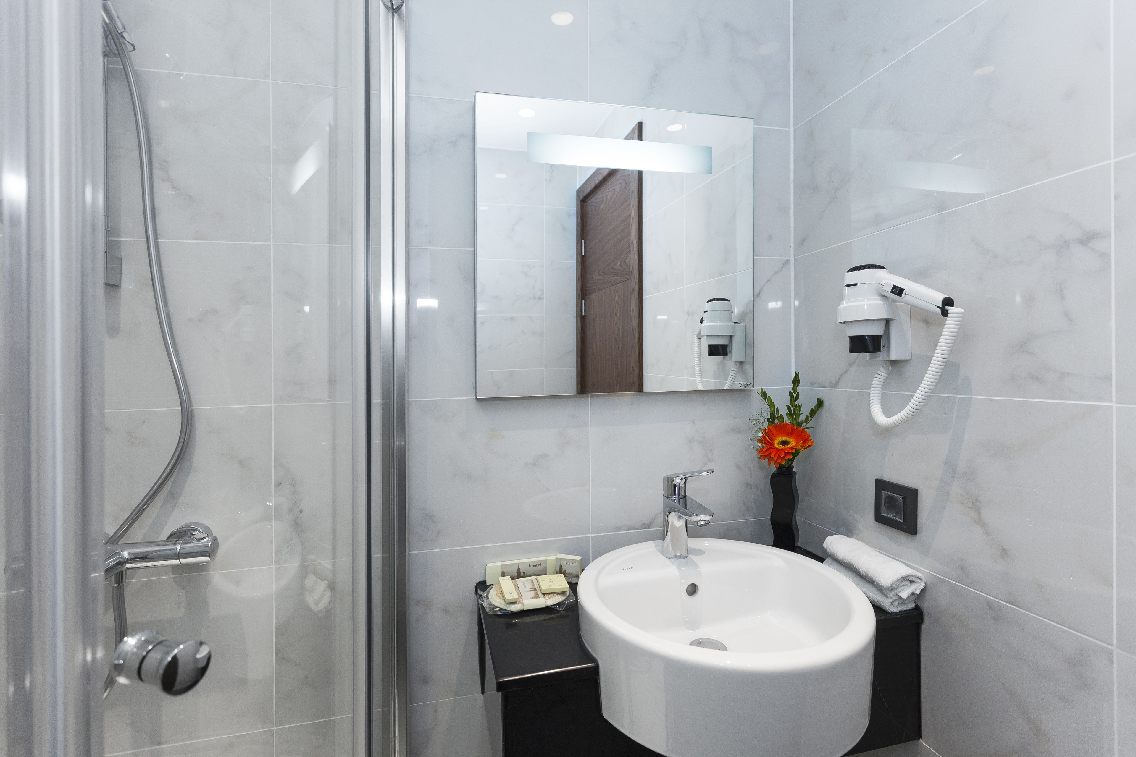 Een moderne badkamer met een douchecabine van glas, een witte wastafel en een spiegel erboven.