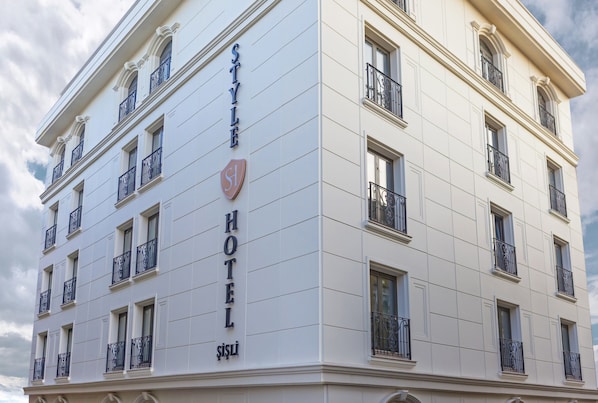 Un hotel de varios pisos con un estilo arquitectónico clásico, que cuenta con balcones con barandillas de hierro forjado y un letrero llamativo que dice "STYLE HOTEL".