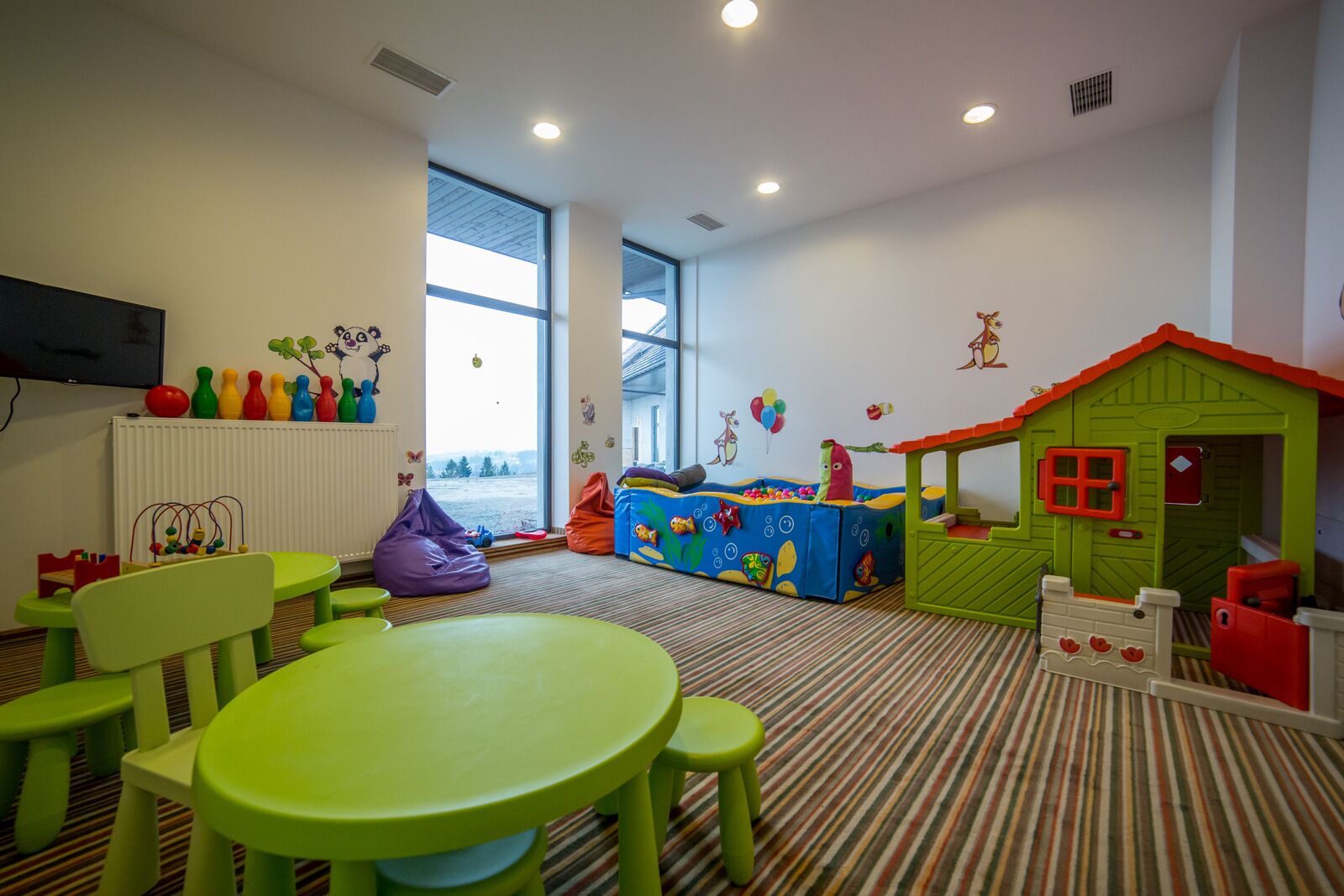 A children's playroom with a large window, a playhouse, and a table with chairs.
