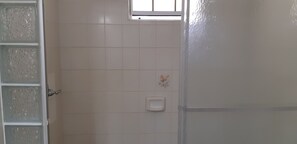 Un baño con paredes de azulejos blancos, una ventana y dispensador de jabón.