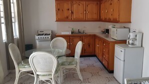 A kitchen with wooden cabinets, a gas stove, a microwave, and a refrigerator. There is a round table with chairs and a glass top. - Leisure Inn (Soufrière)