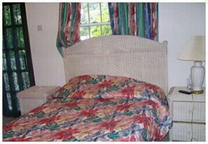 A bed with a floral bedspread, a bedside lamp, and curtains on a window. - Leisure Inn (Soufrière)