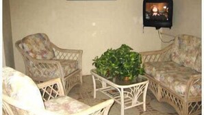 A room with two wicker chairs, a small table with a plant, and a television mounted on the wall. - Leisure Inn (Soufrière)