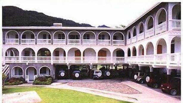 A building with a courtyard, multiple arches, and parked vintage cars. - Leisure Inn (Soufrière)