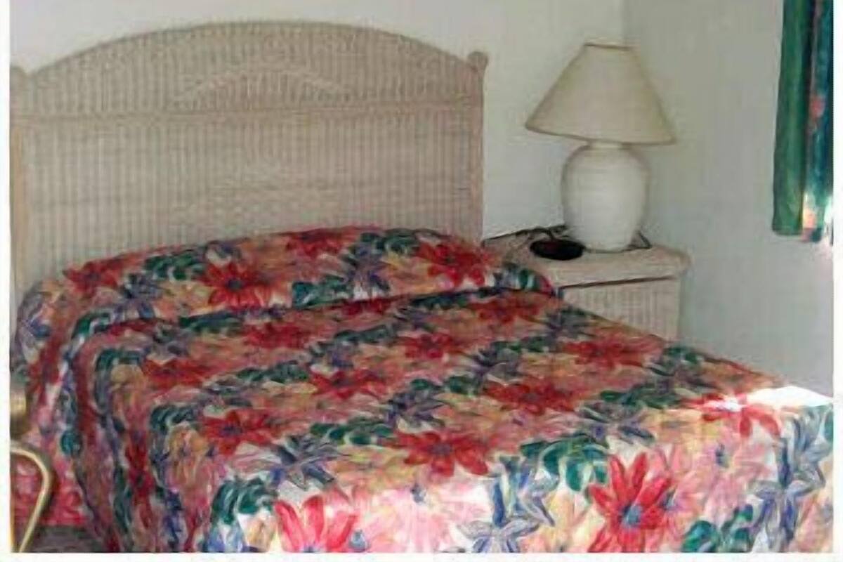 A bed with a floral bedspread, a bedside lamp, and a nightstand with a phone.