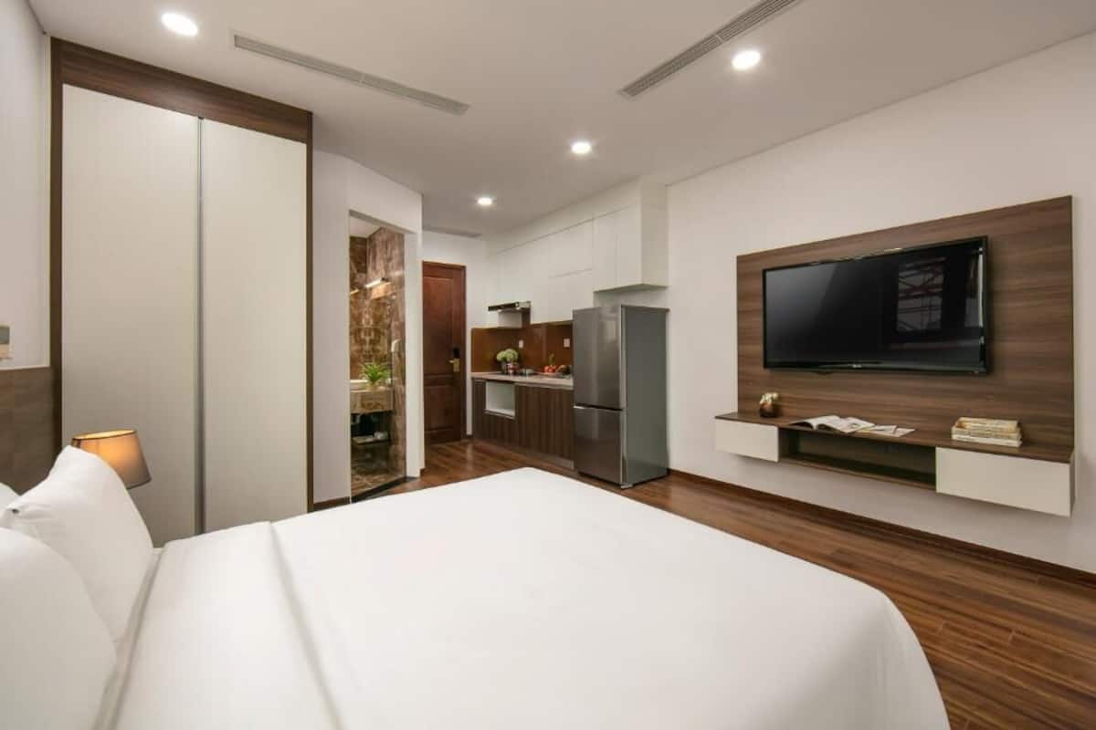 Et moderne hotelværelse med en stor seng, et fjernsyn monteret på væggen, et tekøkken og et walk-in closet.