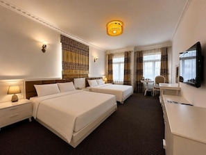 A hotel room with two beds, a desk, a chair, a television, and a patterned wall hanging. - Luxor Boutique Hotel (Hanoi)