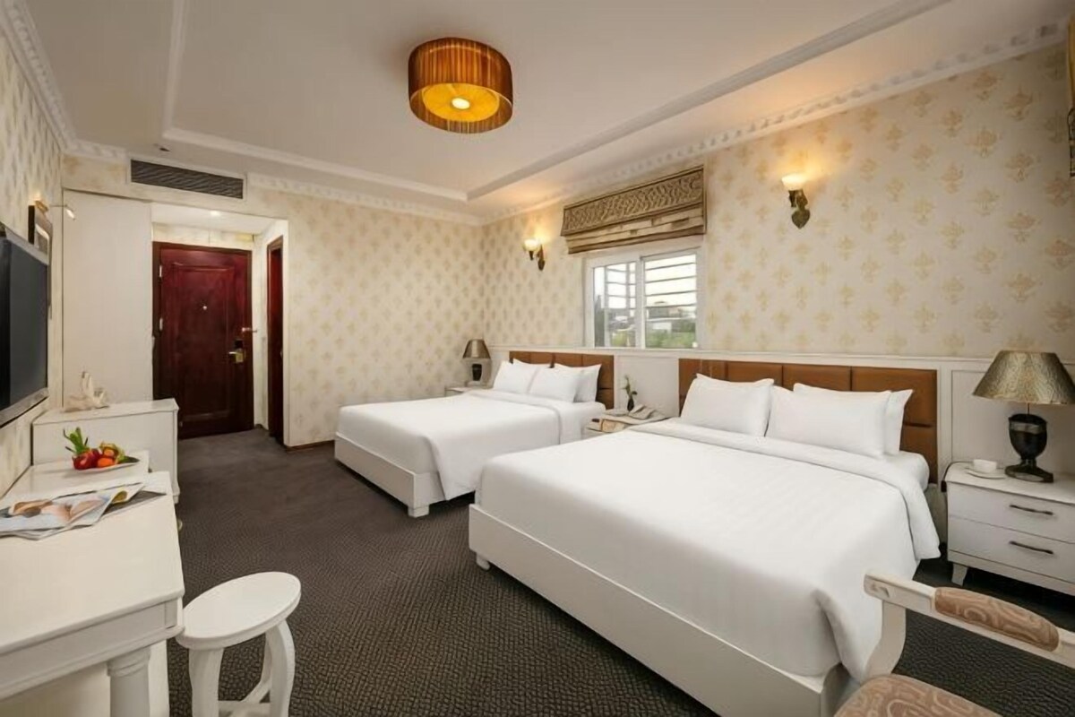 A hotel room with two beds, a desk, a chair, a TV, and a window.