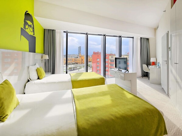 A hotel room with two beds, a desk with a computer, a TV, and a view of the cityscape. - ibis Styles Wroclaw Centrum (Wroclaw)