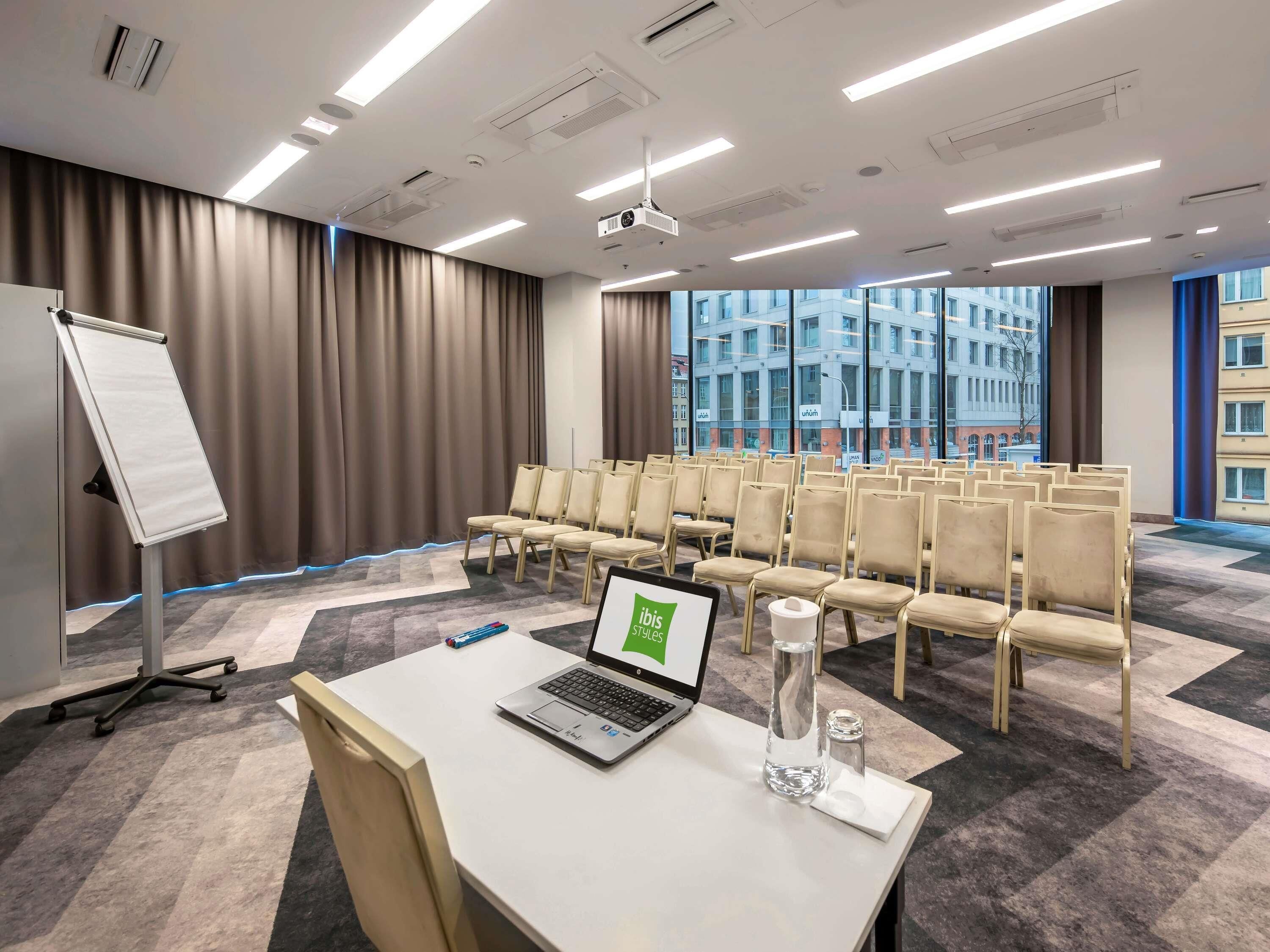 A conference room with a whiteboard, rows of chairs, a laptop, a projector, and a large window with a city view.