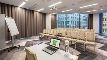 A conference room with a whiteboard, rows of chairs, a laptop, a projector, and a large window with a city view.