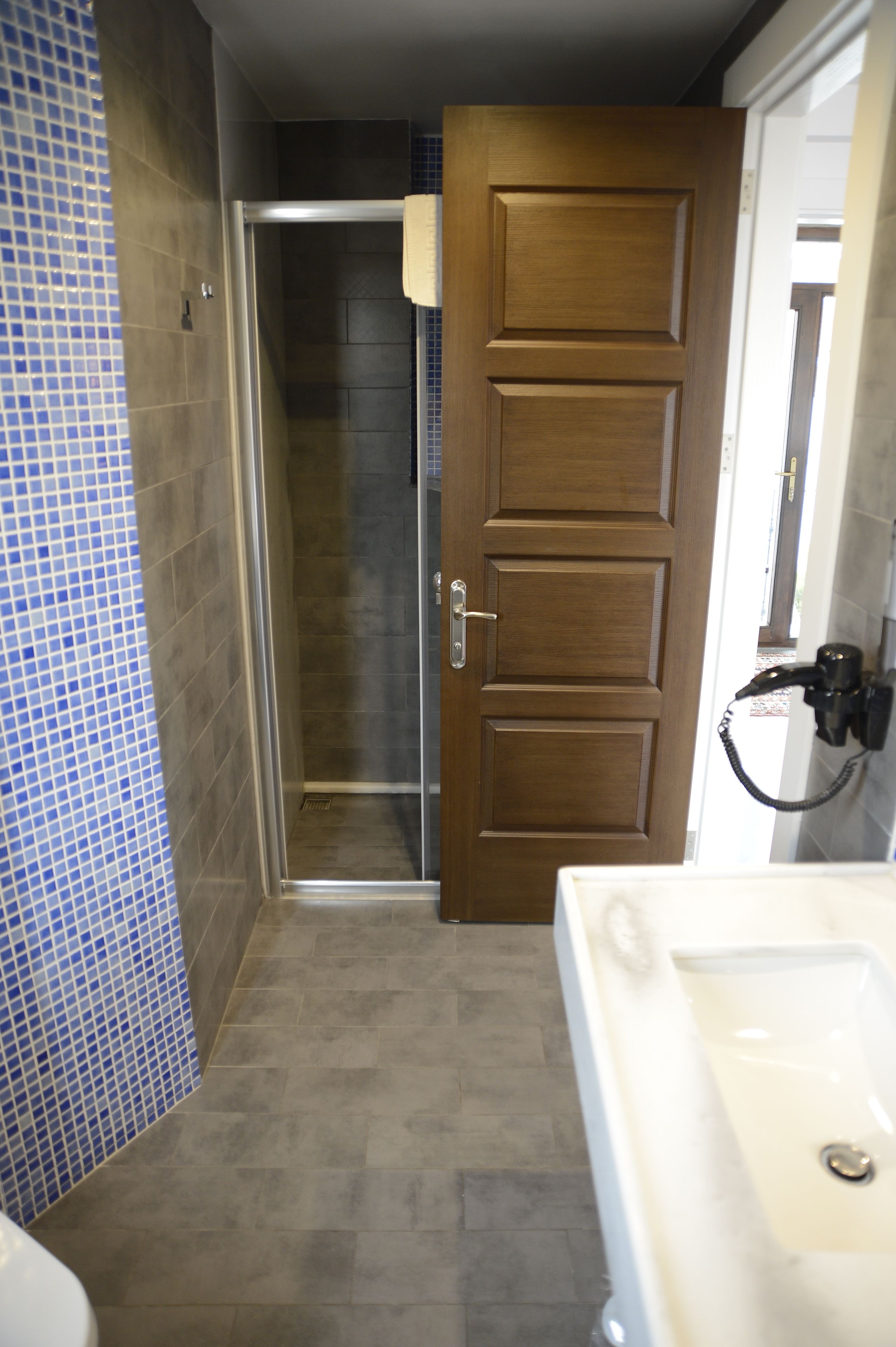 Une salle de bain avec une douche, une porte en bois et un lavabo blanc.