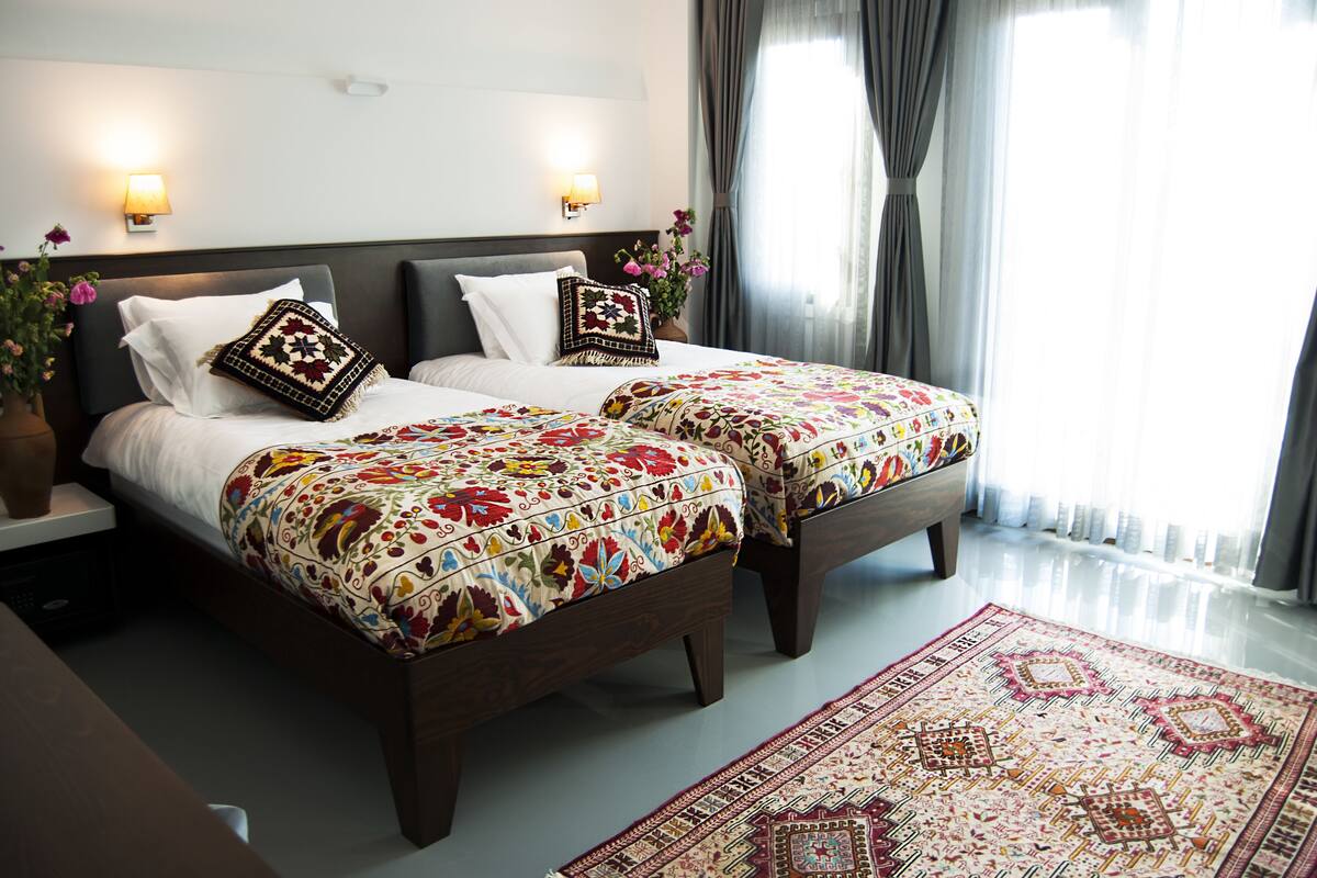A double bed with floral-patterned bedding, two bedside lamps, and a decorative pillow.