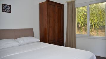 Une chambre à coucher avec un lit, une armoire en bois, une fenêtre avec des rideaux et un élément décoratif mural.