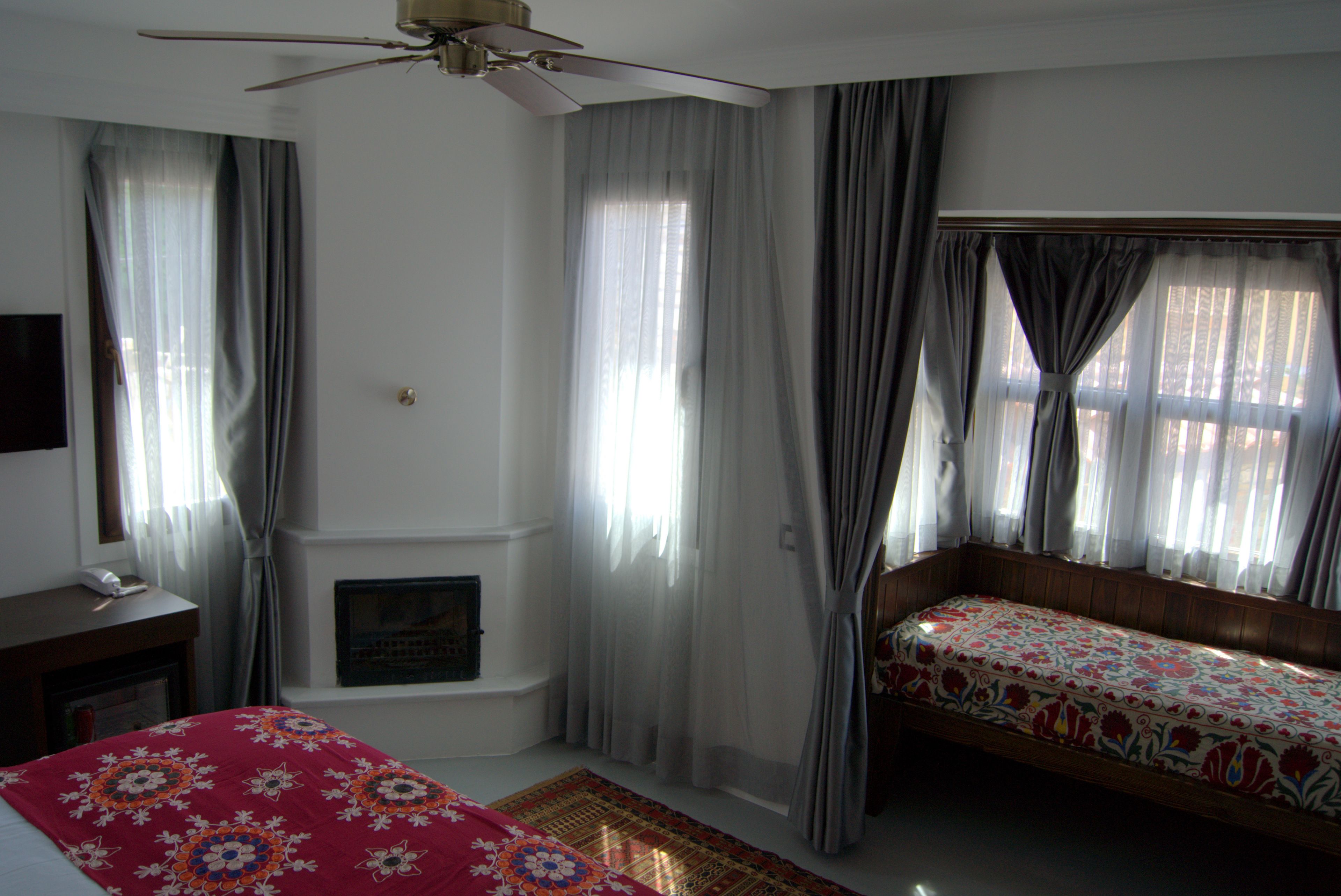 A bedroom with a bed, a fireplace, a ceiling fan, and a window with curtains.