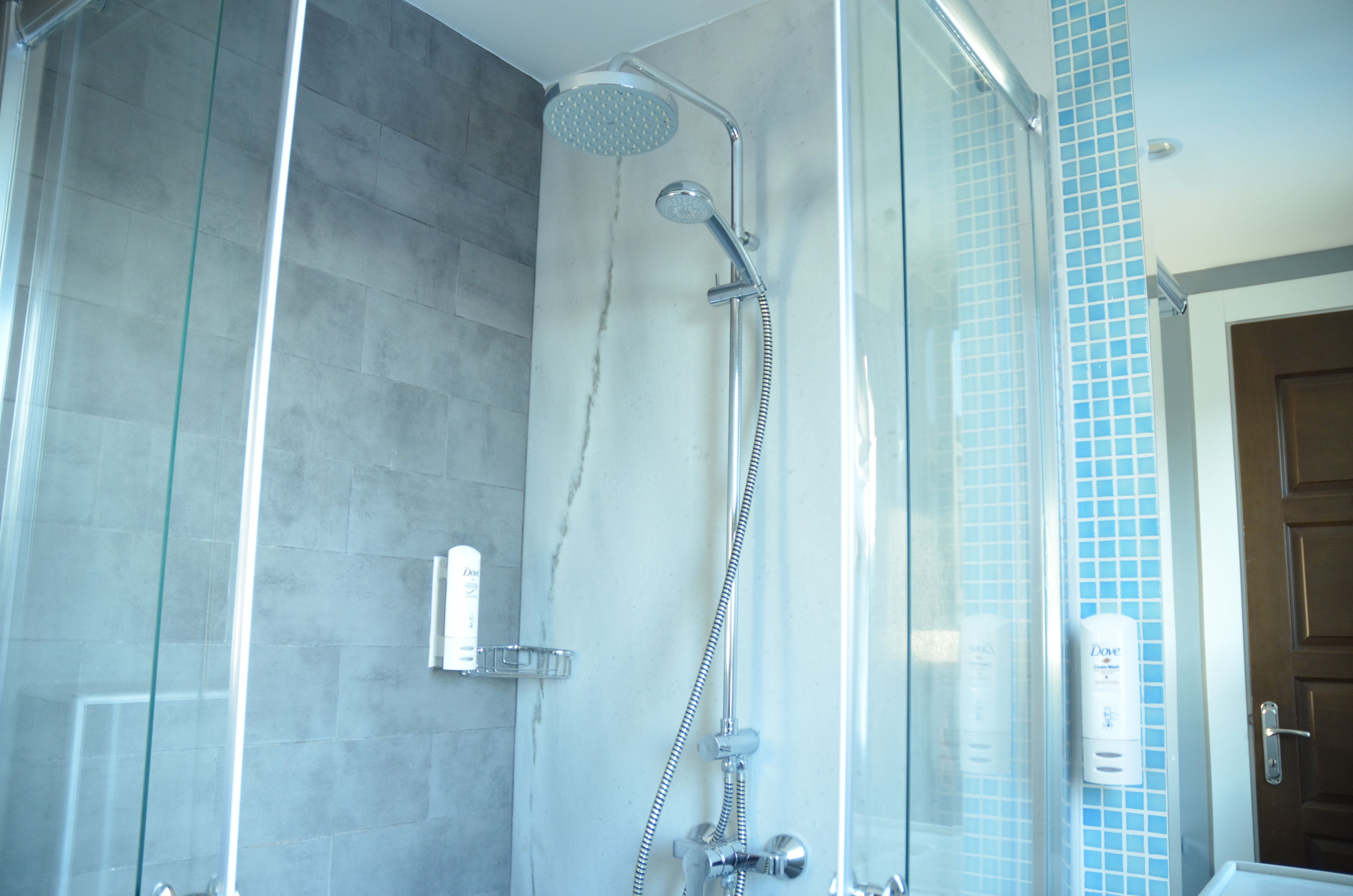 A glass-enclosed shower with a handheld showerhead and a wall-mounted faucet.