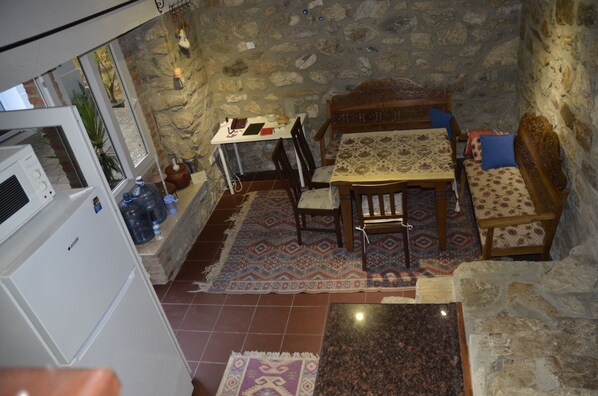 Una habitación con paredes de piedra, una mesa de comedor, sillas y un banco. Incluye un refrigerador, un dispensador de agua y una alfombra estampada.