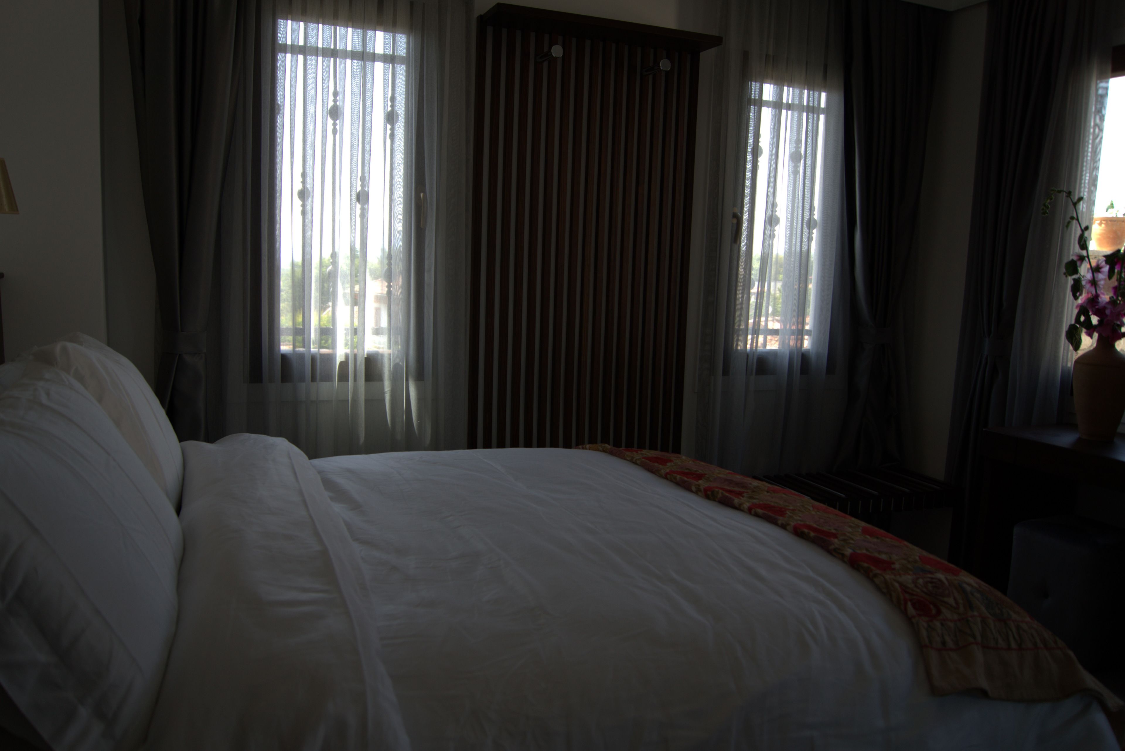 Een hotelkamer met een groot bed, gordijnen en een raam met zonwering.