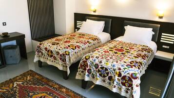 Une chambre d’hôtel avec deux lits, chacun recouvert d’une couvre-lit à motifs, une table de chevet, une petite table et un tapis décoratif.