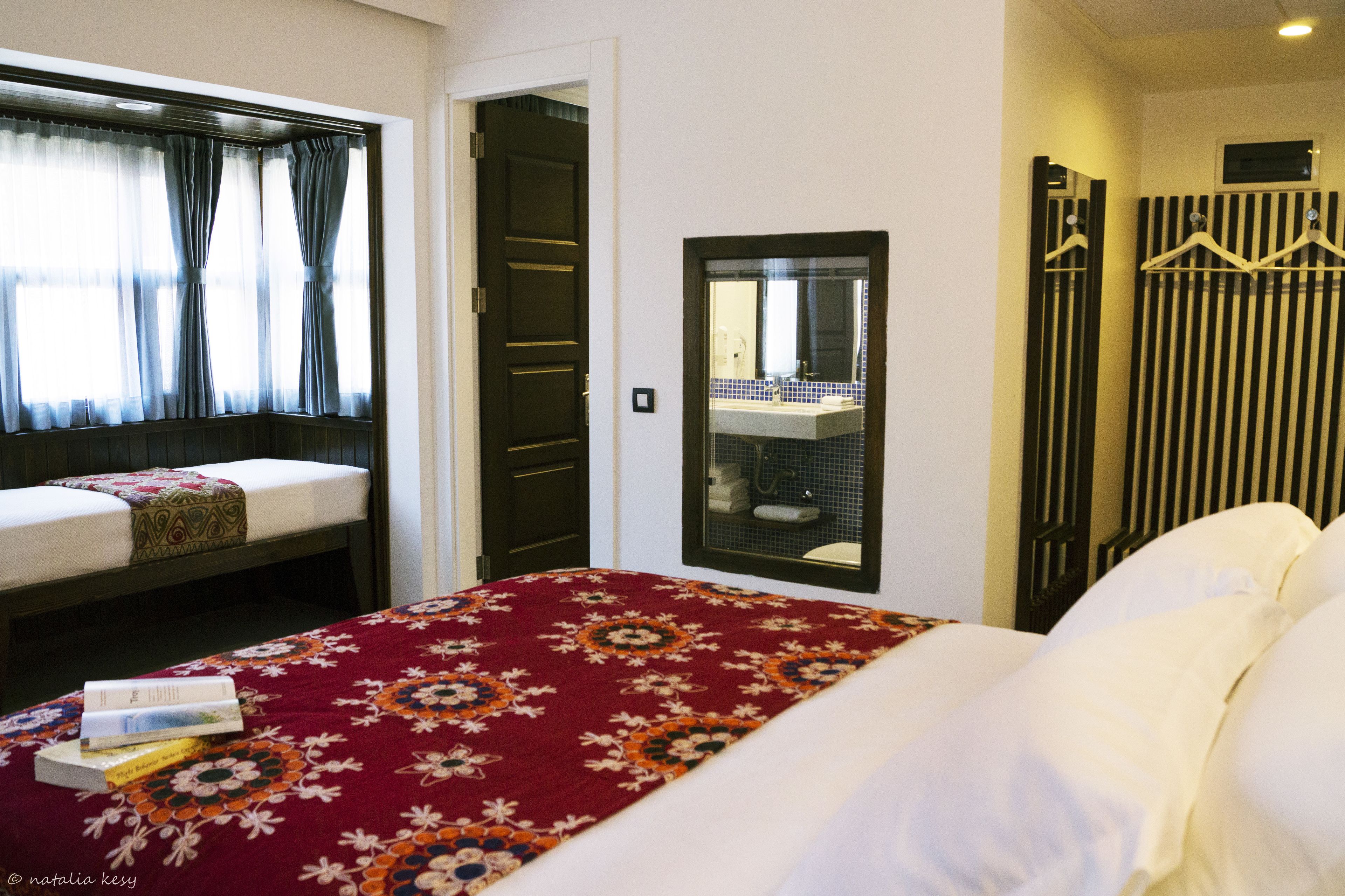A hotel room with a bed, a window with curtains, a door, and a mirror.