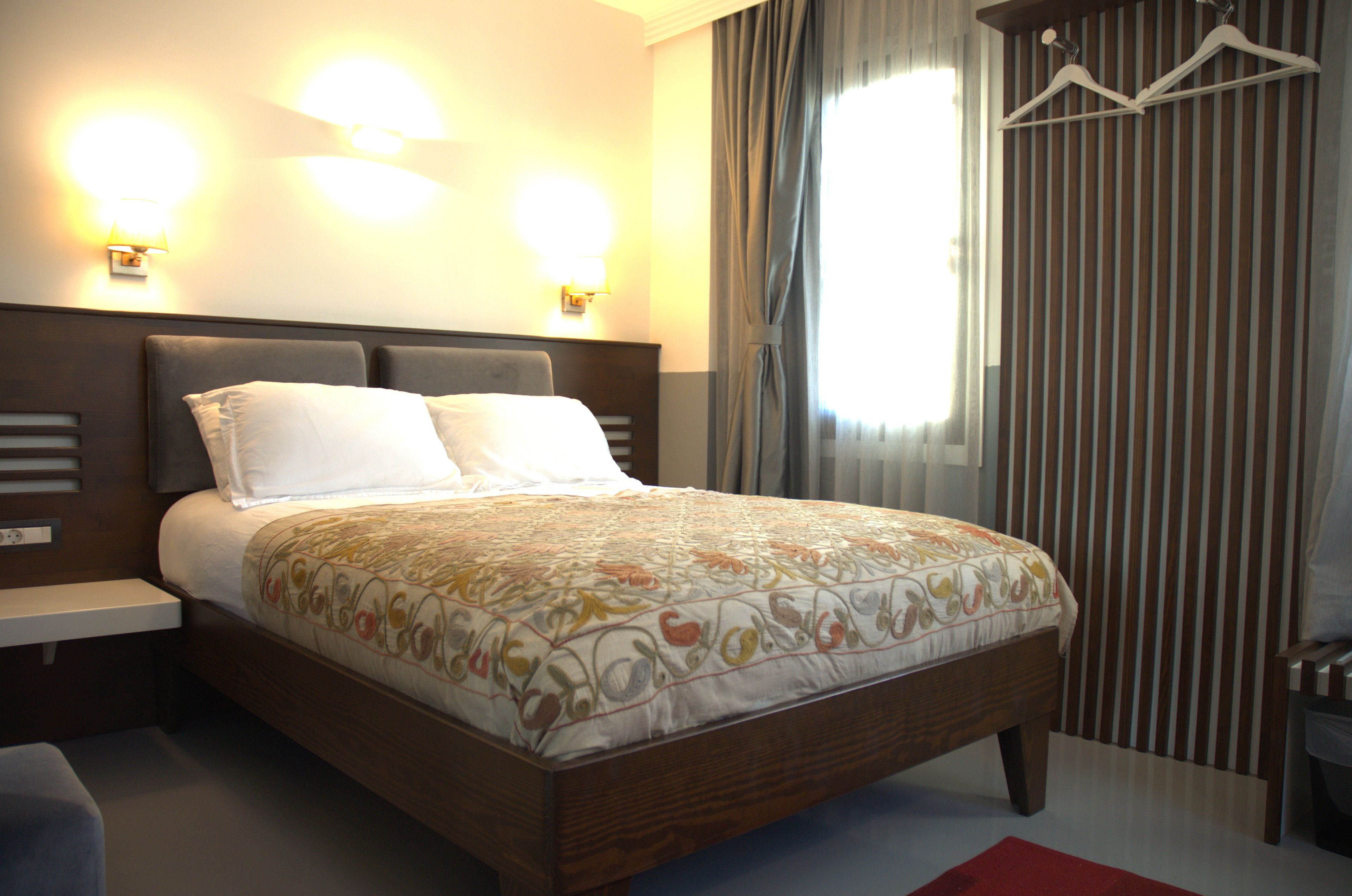 Un lit bien fait, recouvert d’une couvre-lit à motifs, avec deux lampes de chevet et un porte-manteau suspendu.