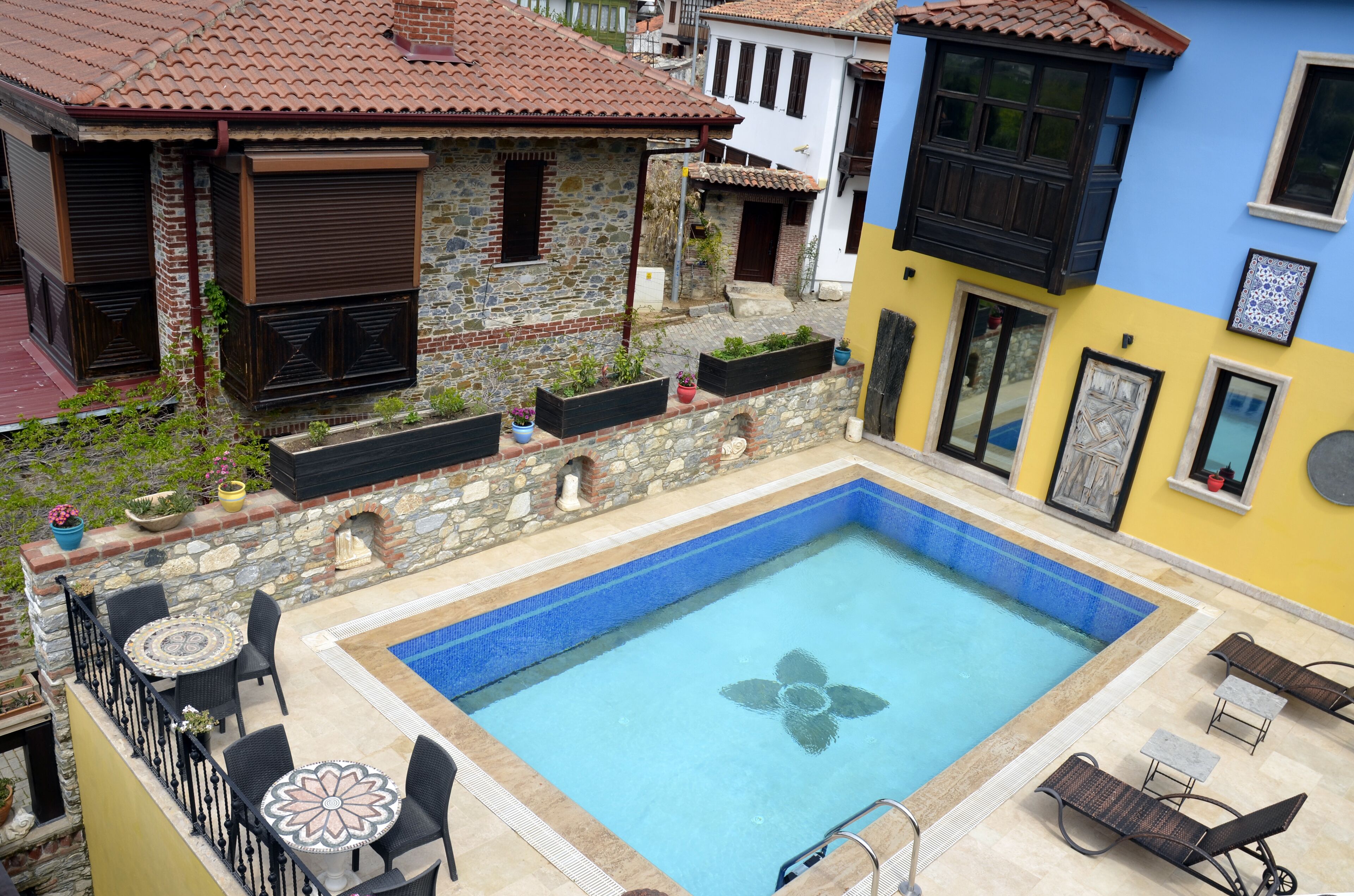 Una piscina en la azotea con diseño floral, rodeada de muros de piedra y plantas en macetas.
