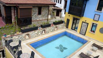 Una piscina en la azotea con diseño floral, rodeada de muros de piedra y plantas en macetas.