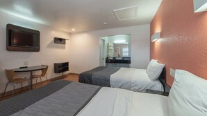 Habitación de hotel con dos camas, un escritorio con silla, televisor y espejo.