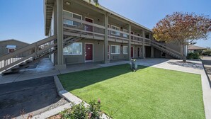 Un motel de varios pisos con una escalera central, un pequeño jardín y un árbol con hojas otoñales.