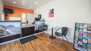 Zona de recepción con suelo de madera, mostrador de recepción, dos sillones, una mesita y un televisor instalado en la pared.