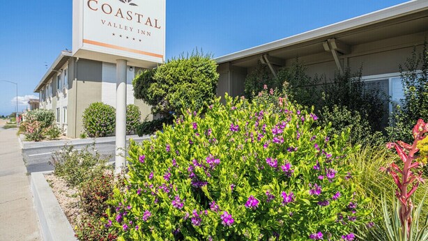 Edificio del Coastal Valley Inn con un letrero, rodeado de follaje y flores bien cuidados.