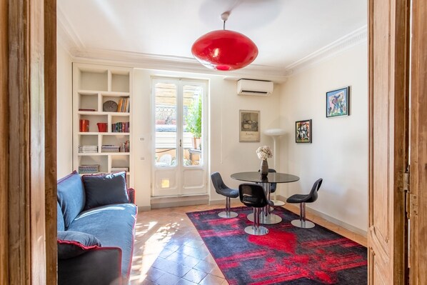 A living room with a blue sofa, a red pendant light, a round table with two chairs, and a red and black rug.