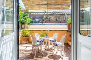 An outdoor patio with a table and four chairs, surrounded by potted plants and a wooden pergola. - Frattina Apartments (Rome)