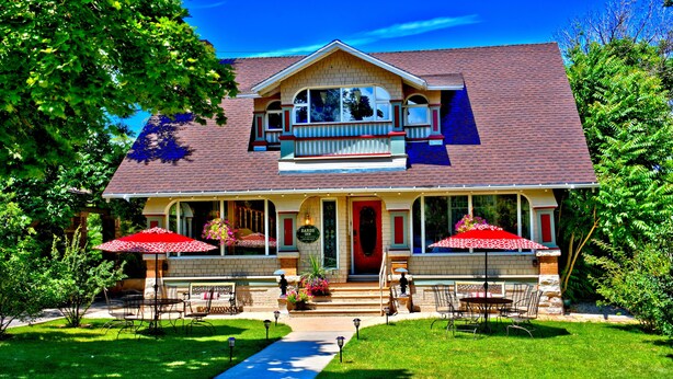 A two-story house with a front porch, a red door, and two umbrellas. - Bard's Inn (Cedar City)