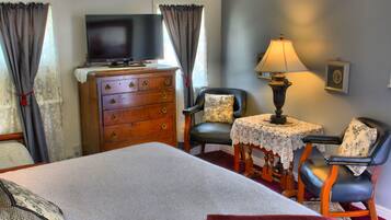 A bedroom with a bed, a dresser, a television, two chairs, a table, and a lamp.