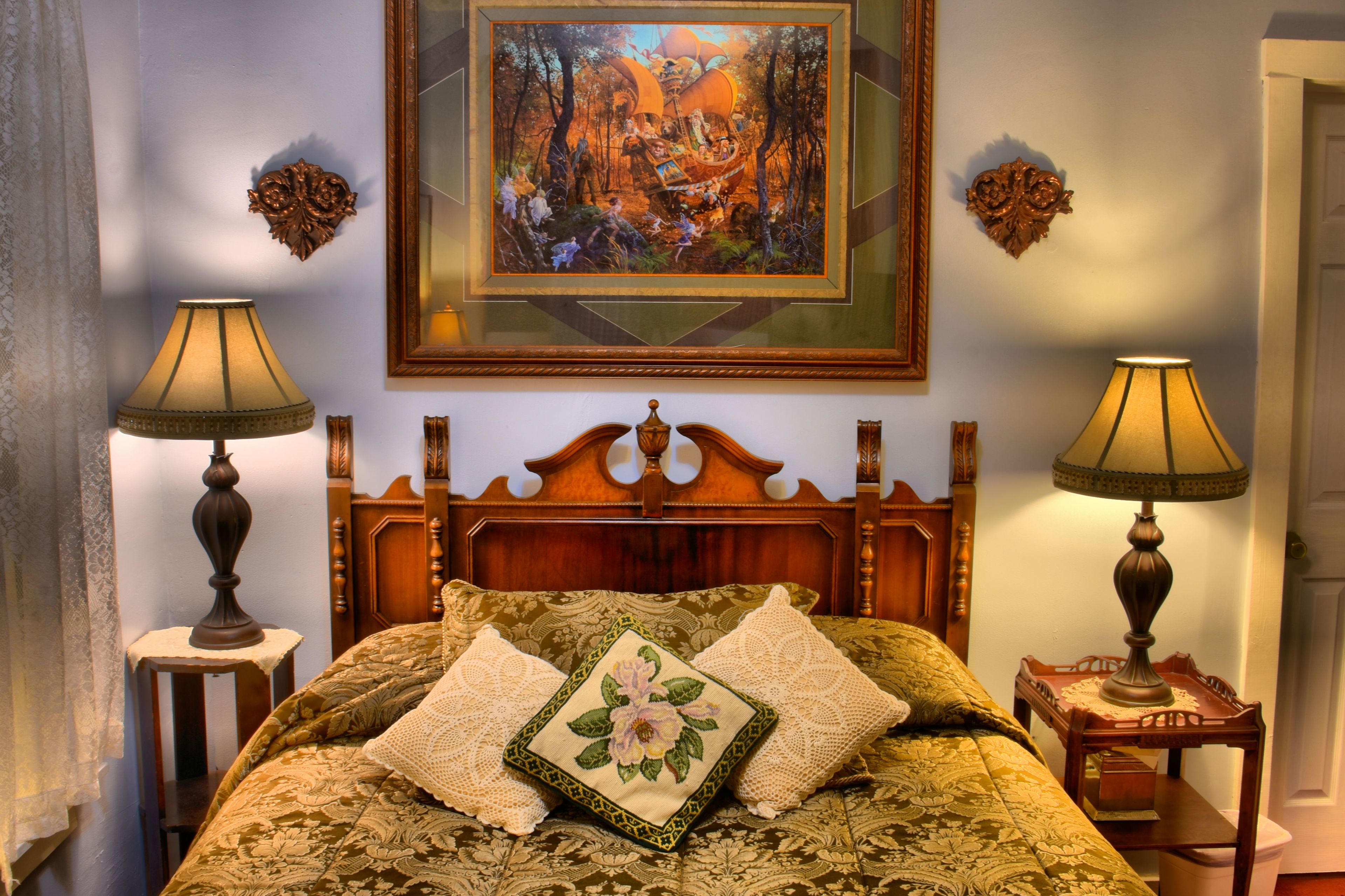 A bedroom with a wooden bed, two bedside lamps, a floral bedspread, and a framed painting on the wall.